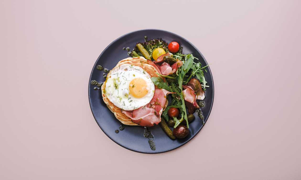 American pancakes with serrano ham, fried egg and pesto sauce, pickles