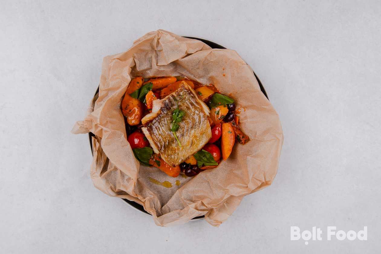 Baked cod in paper with potato, cherry tomatoes, olives and mediterranean sauce