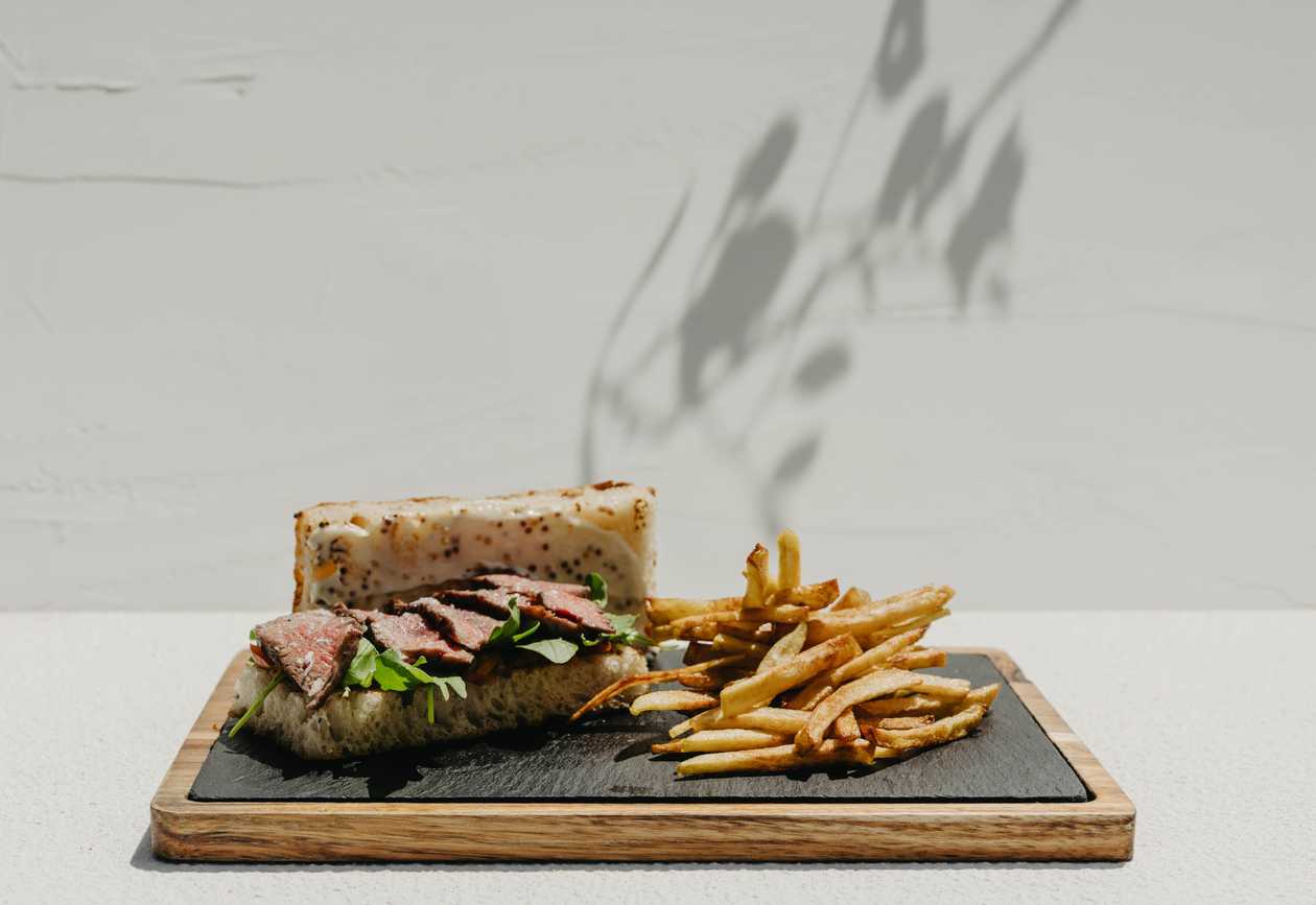 Sandwich cu steak de vită în focaccia cu rucola și roșii cherry, însoțit de cartofi prăjiți