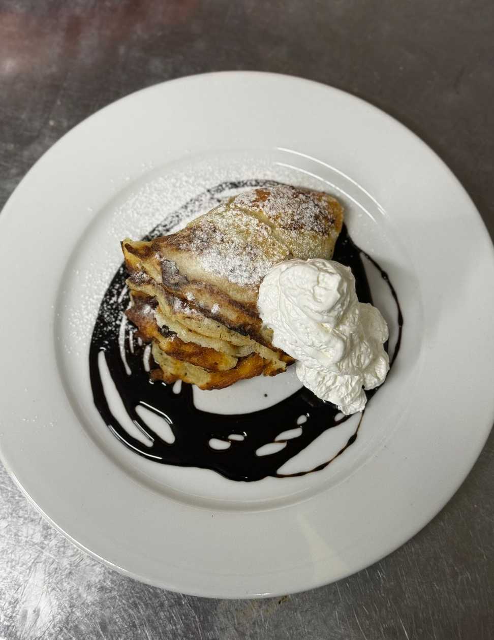 Pancake with jam, ice cream, and chocolate topping, garnished with whipped cream