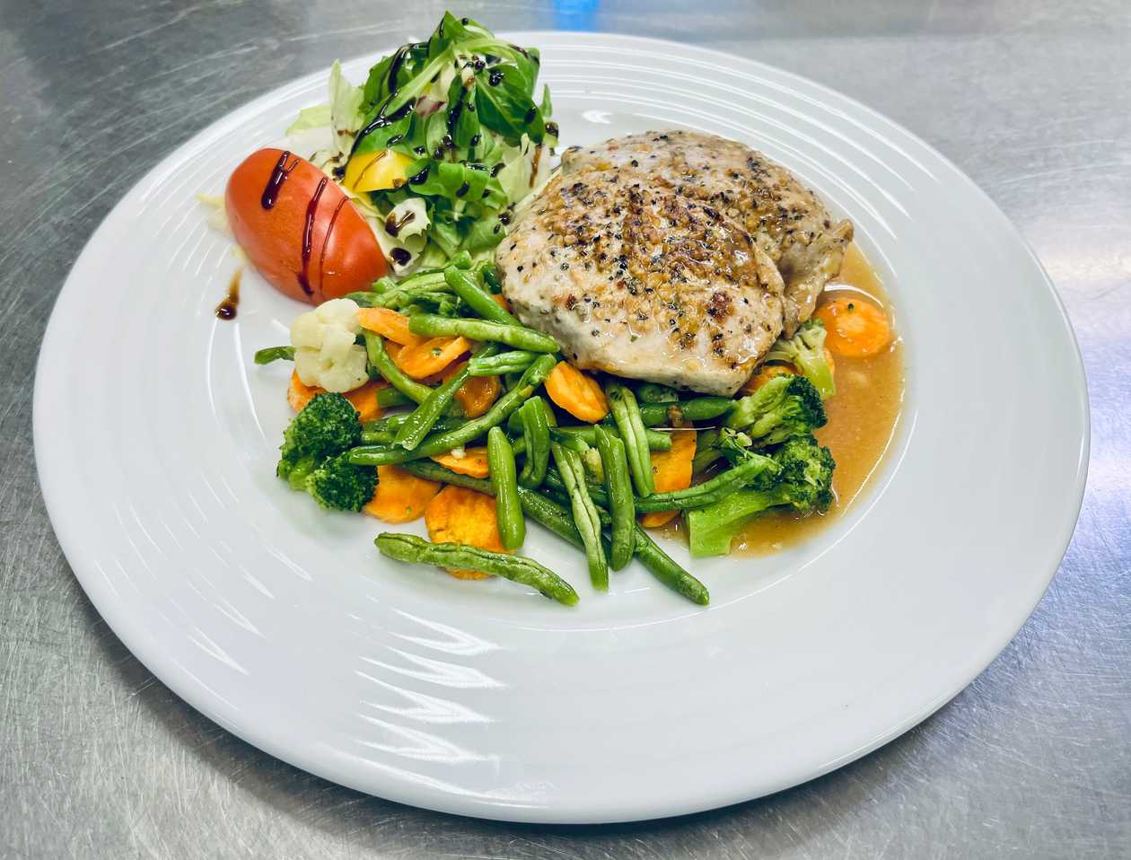 Steak z vepřové kotlety podávaný s baby zeleninou na másle a bylinkách