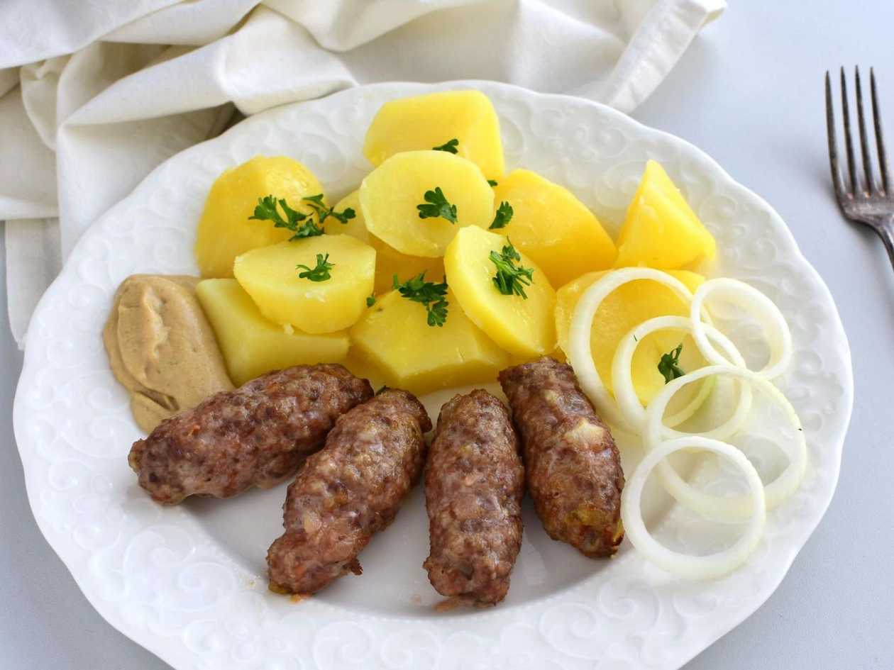 Pečené čevabčiči, vařené brambory, hořčice, cibulka