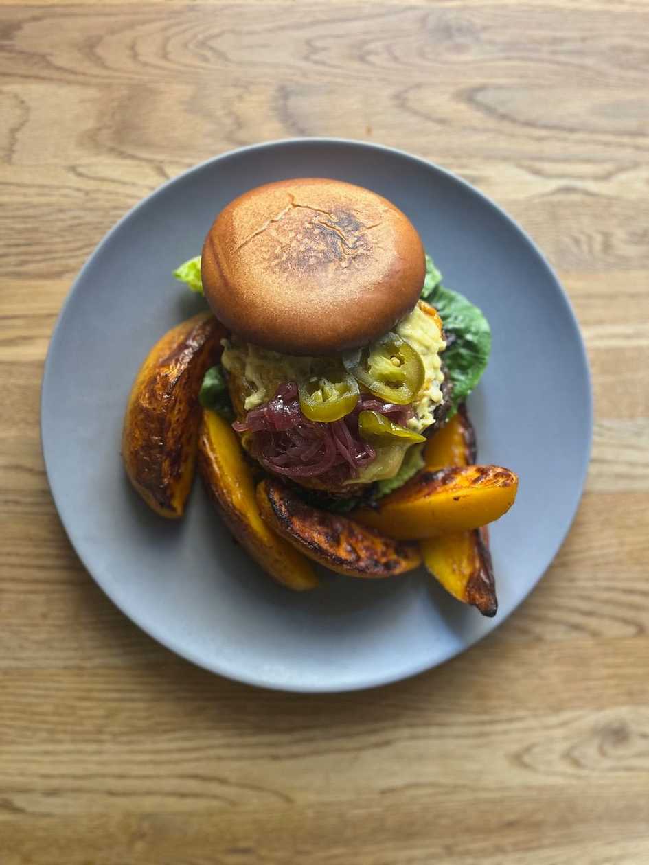 Burger z našeho mletého hovězího masa s domácí česnekovou majonézou, ledovým salátem,jalapeňos, pečenou slaninou a cibulkou, zapečený čedarem