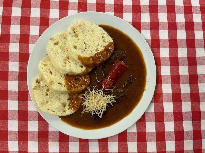 7. 100g. Staropražský hovězí guláš zdobený klobáskou a křenem, houskový knedlík