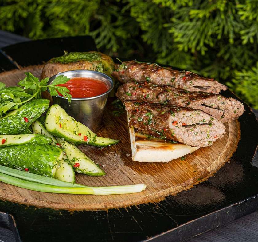 Veal Lula Kebab with Roasted Potatoes, Spicy Butter, Quick Pickled Cucumbers, and Ajika, Served on Pita Bread