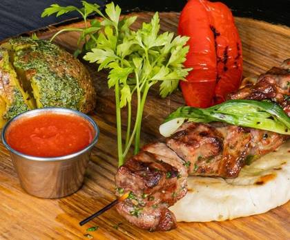 Pork Shashlik with Baked Potato, Herb Butter, Grilled Pepper, Ajika, Served on Pita Bread