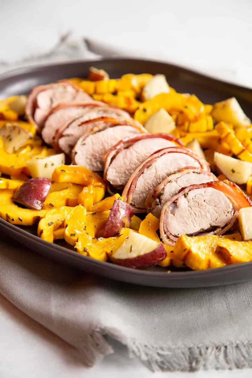 Pork tenderloin wrapped in bacon leaf and green lettuce leaf, topped with whole baked potatoes