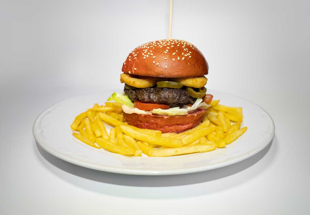 Spicy beef hamburger with jalapeños and onion rings, BBQ sauce, mayonnaise, tomato, salad, french fries
